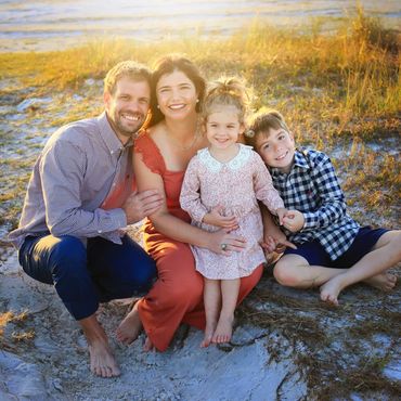 Happy family of four sitting together on a sandy beach at sunset.