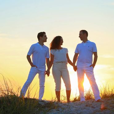 Three people holding hands at sunset on a sandy hill.
