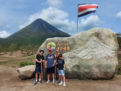 Un grupo de 4 personas posando junto a una roca con un volcán de fondo