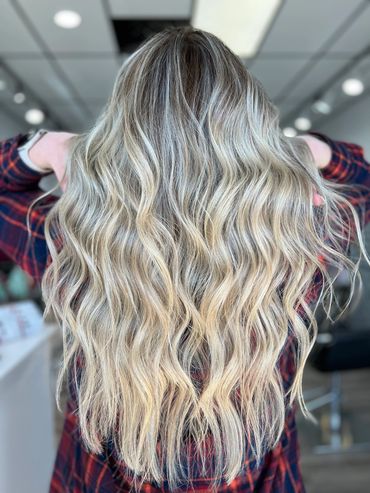 Long wavy blonde hair with dark roots in an indoor setting.