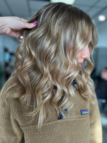Wavy, highlighted blonde hair styled on a woman in a cozy brown sweater.