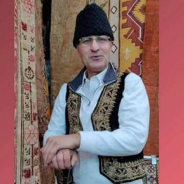 Tom wearing a traditional Persian hat. standing in front of beautifully patterned rugs