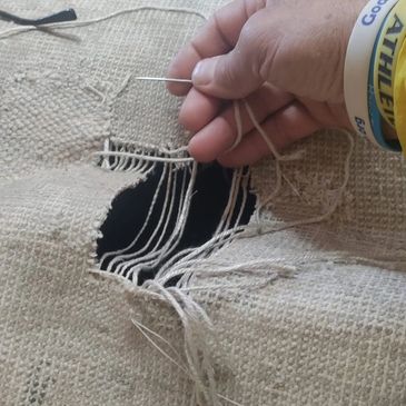 tom using a needle to hand repair a rug with a large section missing