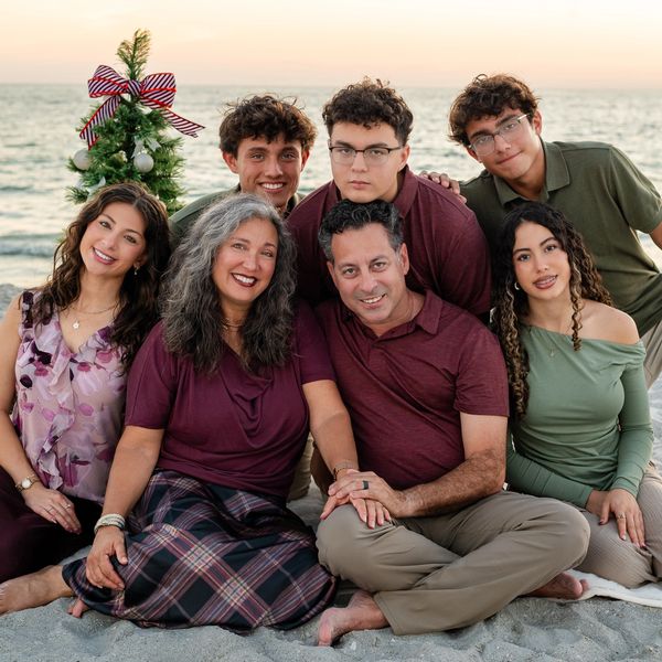A happy family poses on the beach with a small decorated Christmas tree at sunset.