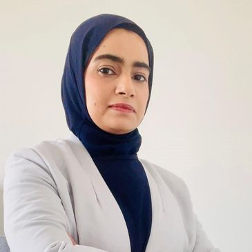 Confident woman wearing a navy hijab and white blazer posing with crossed arms.
