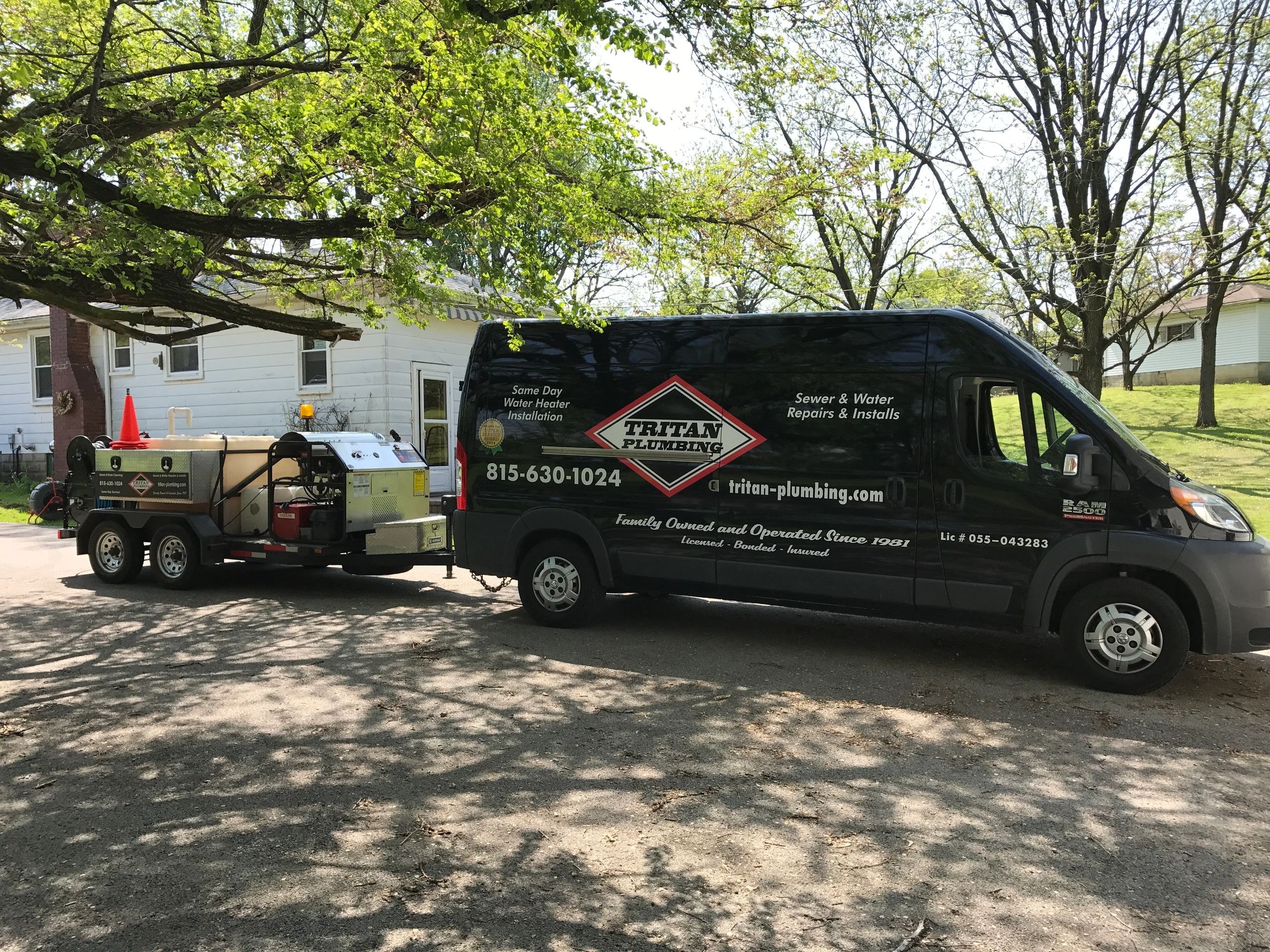 Tritan Plumbing van with our Jetter trailer parked on a residential street under trees on a emergency drain service call.