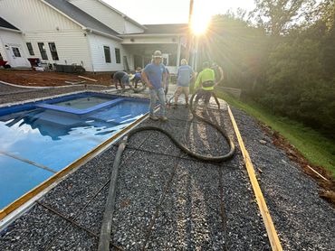 Workers pouring concrete near a pool at sunset.