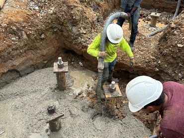 Construction workers pouring and leveling concrete in a foundation pit.