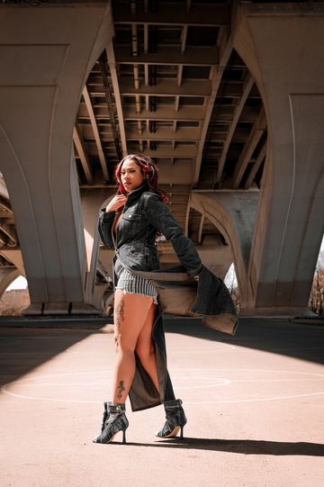 Fashionable woman posing confidently under a bridge in stylish outfit.