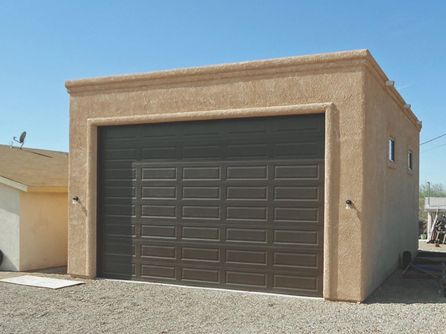 A standalone garage with a large dark garage door and beige stucco walls.