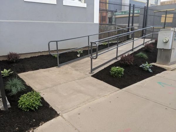Concrete ramp with metal railing beside a building and landscaped plants.