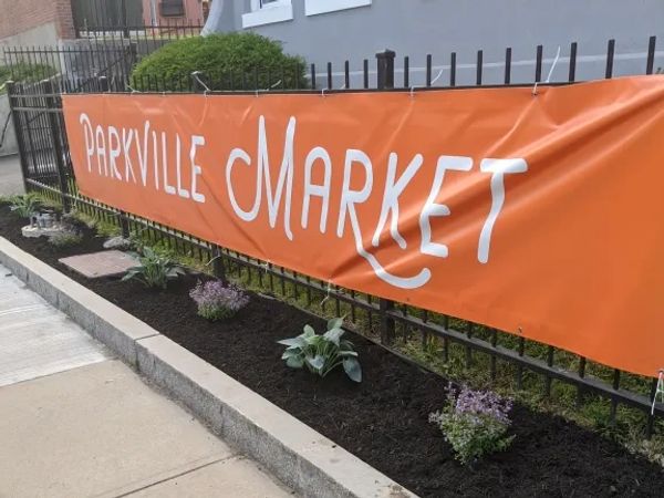Orange banner reading 'Parkville Market' on a black metal fence with small plants.