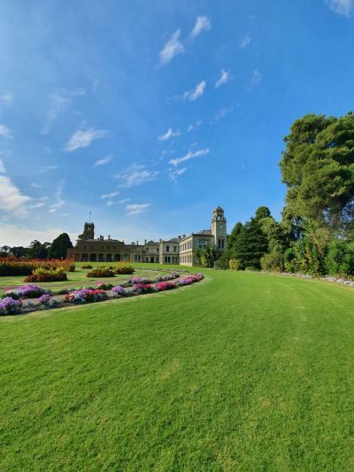 Historic mansion with lush gardens under a clear blue sky.