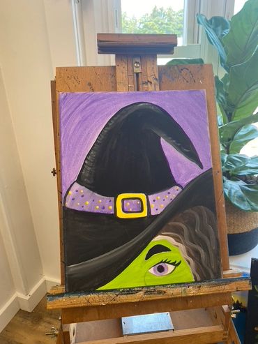 Painting of a green-skinned witch with a purple eye and a black hat.