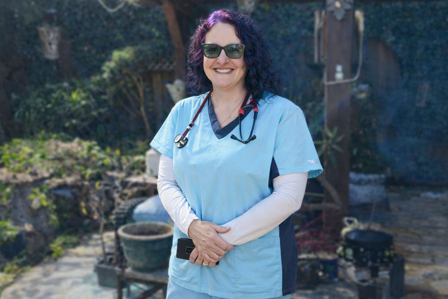 Smiling healthcare worker in blue scrubs outdoors.