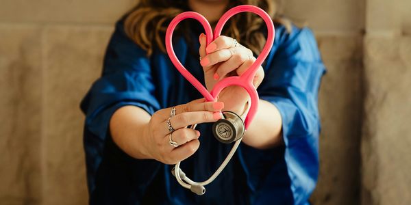 Person holding a pink stethoscope shaped like a heart.