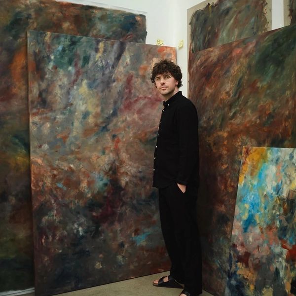 Man standing next to large abstract paintings.