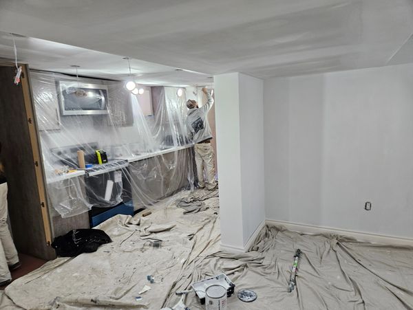 Worker taking a break in a prepped kitchen, seated on a radiator with a drink.