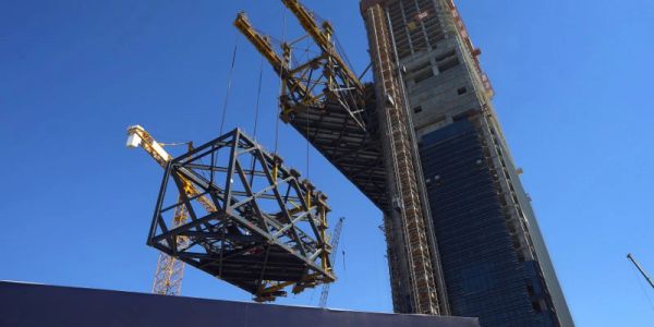 Construction crane lifting a large metal framework near a tall building.