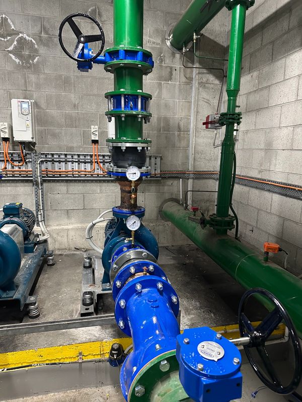 Industrial water pipes with pressure gauges and valves in a utility room.