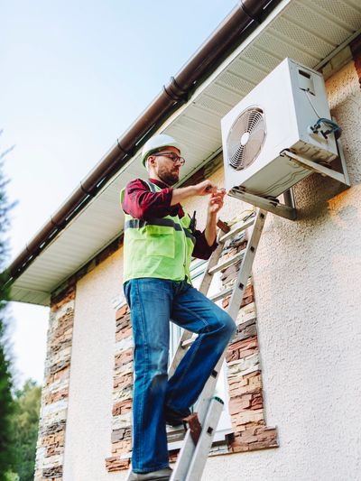 Technician installing an outdoor AC unit on the side of a stucco house.