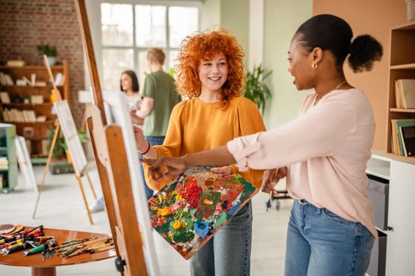 Two women happily painting together in an art studio.