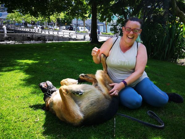 Woman laughing while playing on grass with a happy dog.