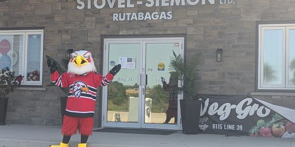 Mascot in red eagle costume stands outside a building entrance with raised arms.