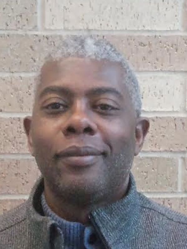Portrait of a smiling middle-aged man with gray hair against a brick wall.