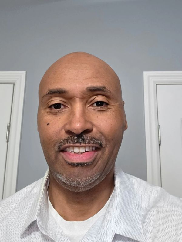 Smiling bald man with a mustache and goatee wearing a white shirt.
