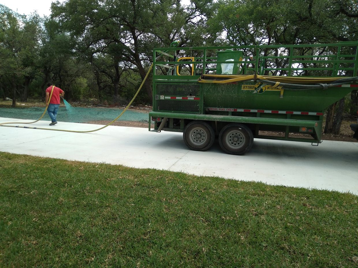 Man spraying hydro mulch from a green trailer.