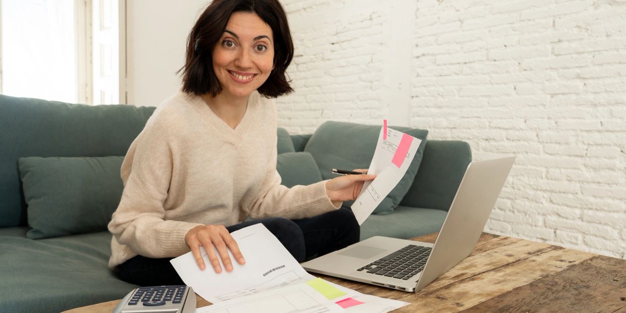 Smiling woman organizing bills and using a laptop.