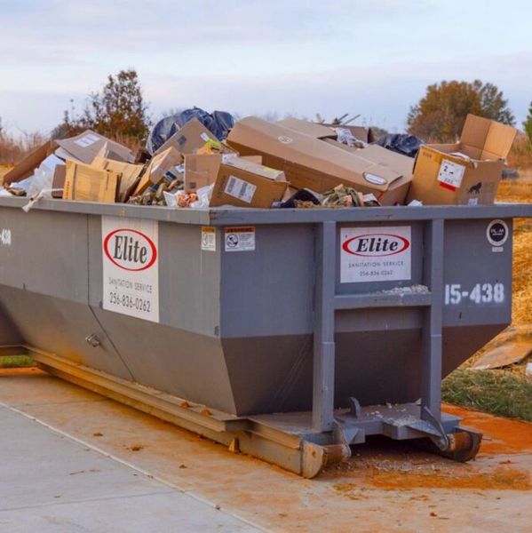 A large gray dumpster filled with cardboard boxes and trash outdoors.