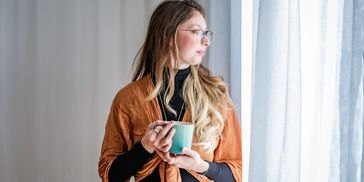 Woman in glasses holding a mug, looking out the window.