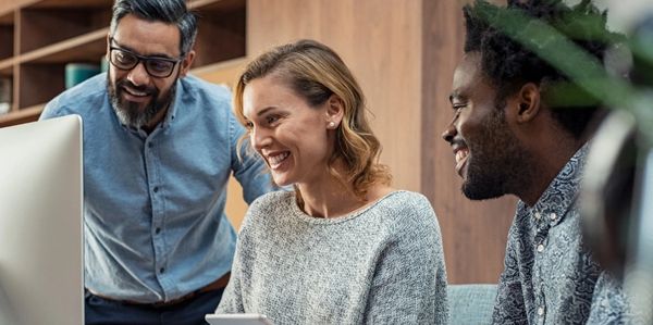 Three colleagues happily collaborating around a computer screen.