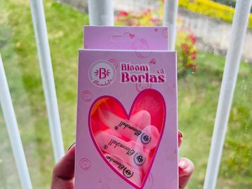 Hand holding a pink box of Bloom Borlas by Bloomshell with a heart-shaped window.