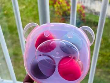 Hand holding a transparent bear-shaped case with colorful makeup sponges.