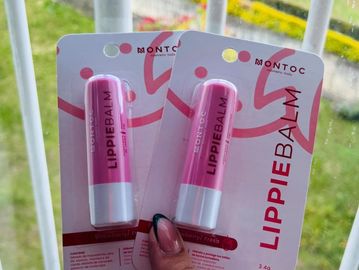 Hand holding two packs of Montoc Lippie Balm lip care products.
