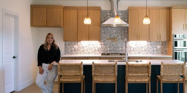 Woman standing in modern kitchen with wooden cabinets and island.