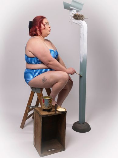 Woman in blue polka dot swimsuit painting a pipe with a bird's nest on top.