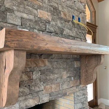 Rustic wooden mantel on stone fireplace wall in a cozy room.