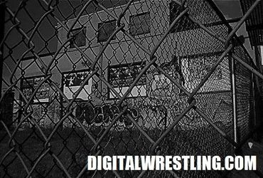 Black and white photo of a graffiti-covered building behind a chain-link fence.