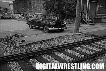 Black vintage car parked near railroad tracks in an old neighborhood.