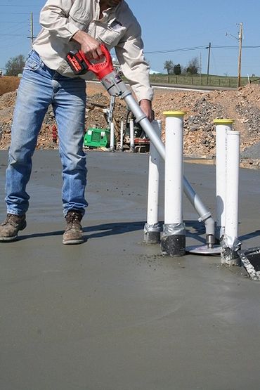 Construction worker uses a power tool on wet concrete around pipes.