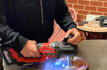 Person using a red power tool to polish a table surface.