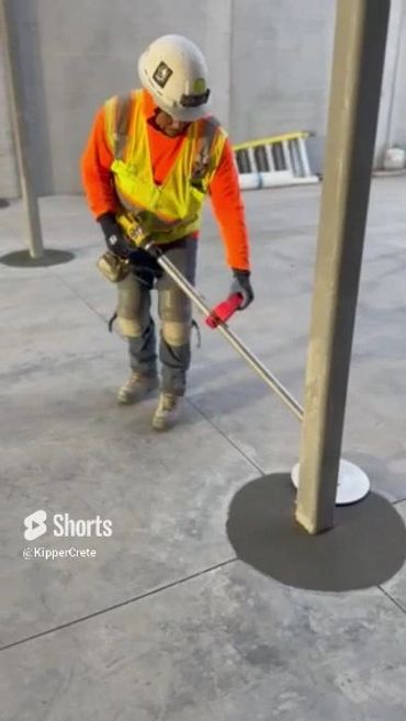 Worker smoothing concrete around a pole on a construction site.