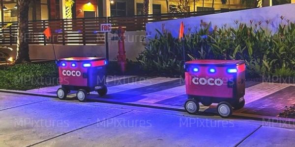 Two small delivery robots with blue lights outside at night.