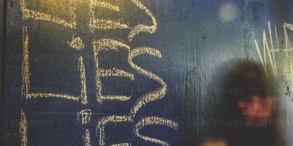 Graffiti on a wall reads 'LIES' repeatedly with a blurred person in the background.
