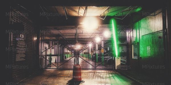 Dimly lit gated parking area with a glowing green light on the right wall.