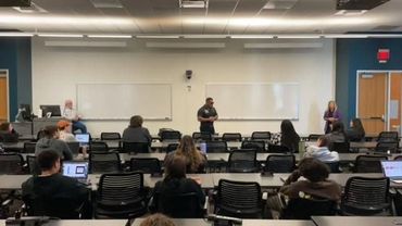 A classroom with a few students and a presenter at the front.